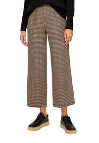 Pantalon à jambes larges à carreaux marron et beige avec poches avant, associé à des baskets noires avec une semelle épaisse couleur caramel.