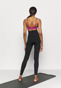 Černé legíny s vysokým pasem a fuchsiová sportovní podprsenka s tenkými ramínky. Legíny jsou hladké a podprsenka má na zádech emblém.