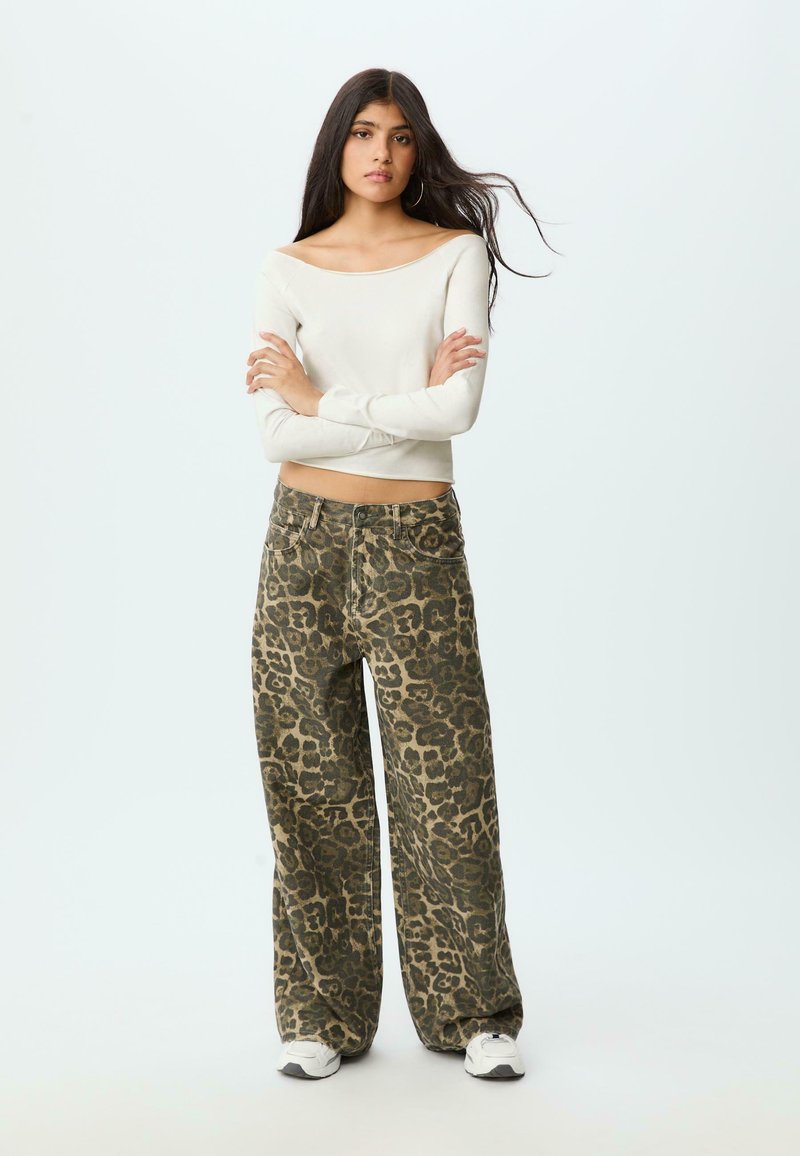 Vit off-shoulder långärmad topp kombinerad med vida olivgröna byxor med svart leopardmönster. Sneakers med gummisula.