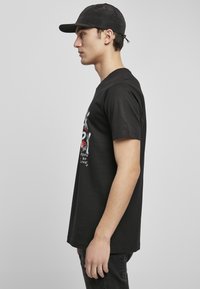 Camiseta negra con un estampado gráfico que presenta texto en blanco y rojo. Tiene mangas cortas y un corte relajado, hecha de suave tela de algodón.