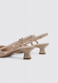 Sandalias tipo slingback beige con un acabado brillante, tacón bajo acampanado, correa ajustable y diseño de tiras cruzadas para mayor soporte y estilo.