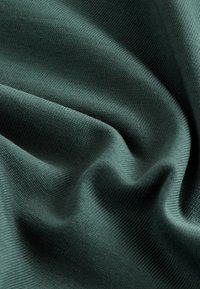Dark green fabric, textured with a ribbed pattern, drapes elegantly with soft, smooth folds, highlighting its stretch and flexibility.