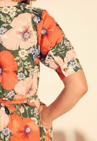 Blumenkleid mit großen orangen Mohnblumen und kleinen blauen Blumen auf grünem Hintergrund. Kurze Ärmel und ein taillierter Schnitt. Glatte Textur.