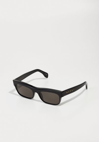 Gafas de sol rectangulares negras con lentes oscuros, montura ancha y logo dorado "MARNI" en la patilla. Material de plástico suave, diseño minimalista.