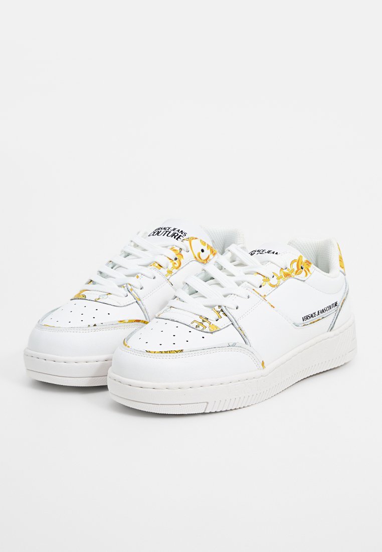 Zapatillas de cuero blancas con un estampado de cadena dorada, puntera perforada, cordones y suela de goma texturizada. Logo impreso en el costado.