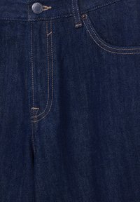 Zbliżenie na przód ciemnoniebieskich dżinsów z denimu z metalowym guzikiem, widoczną przednią kieszenią i kontrastującym pomarańczowym przeszyciem.