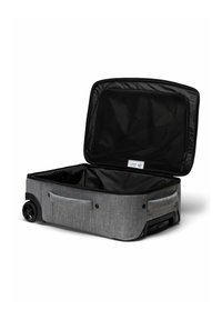 Valise souple grise à roulettes avec un couvercle ouvert, montrant un compartiment en filet zippé à l'intérieur.