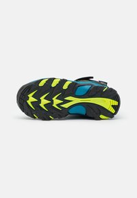 Children's sport shoe with a blue textile upper, black outsole, and bright yellow rubber traction details. Features adjustable strap closure.