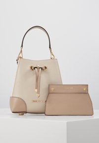 Sac seau en cuir beige avec des accents marron, quincaillerie dorée, fermeture à cordon, et un petit portefeuille assorti. Caractéristiques d'un matériau texturé.