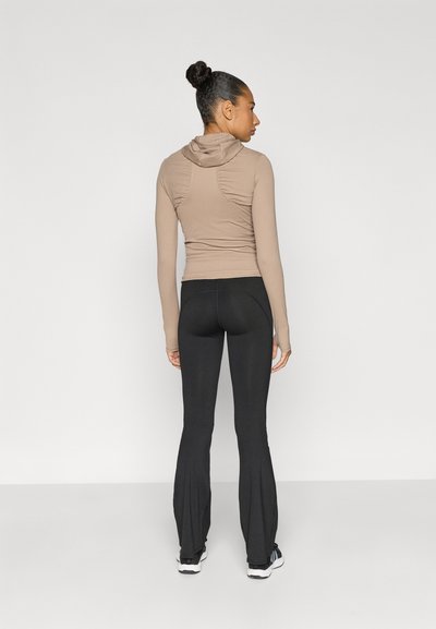 Εφαρμοστή, μακρυμάνικη, μπεζ φούτερ με μικρή κουκούλα και ραμμένη πλάτη, συνδυασμένη με μαύρα, φουσκωτά κολάν με ριγωτή υφή.