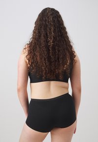 Black cotton sports bra and matching boyshorts, featuring a seamless design and soft texture, viewed from the back on a neutral background.