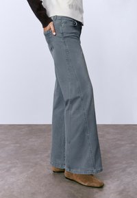 Jeans de pierna ancha gris hechos de denim, con un lavado ligeramente descolorido, bolsillos laterales y detalles de costura a lo largo de las piernas.