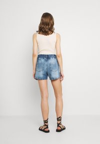Shorts de mezclilla en azul claro con cintura alta y cinturilla elástica. Cuenta con dos bolsillos traseros y un dobladillo ligeramente deshilachado.