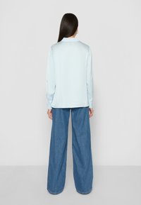 Blusa in satin blu chiaro con colletto, maniche lunghe e taglio dritto, abbinata a jeans in denim blu a gamba larga. Texture liscia e vestibilità rilassata.