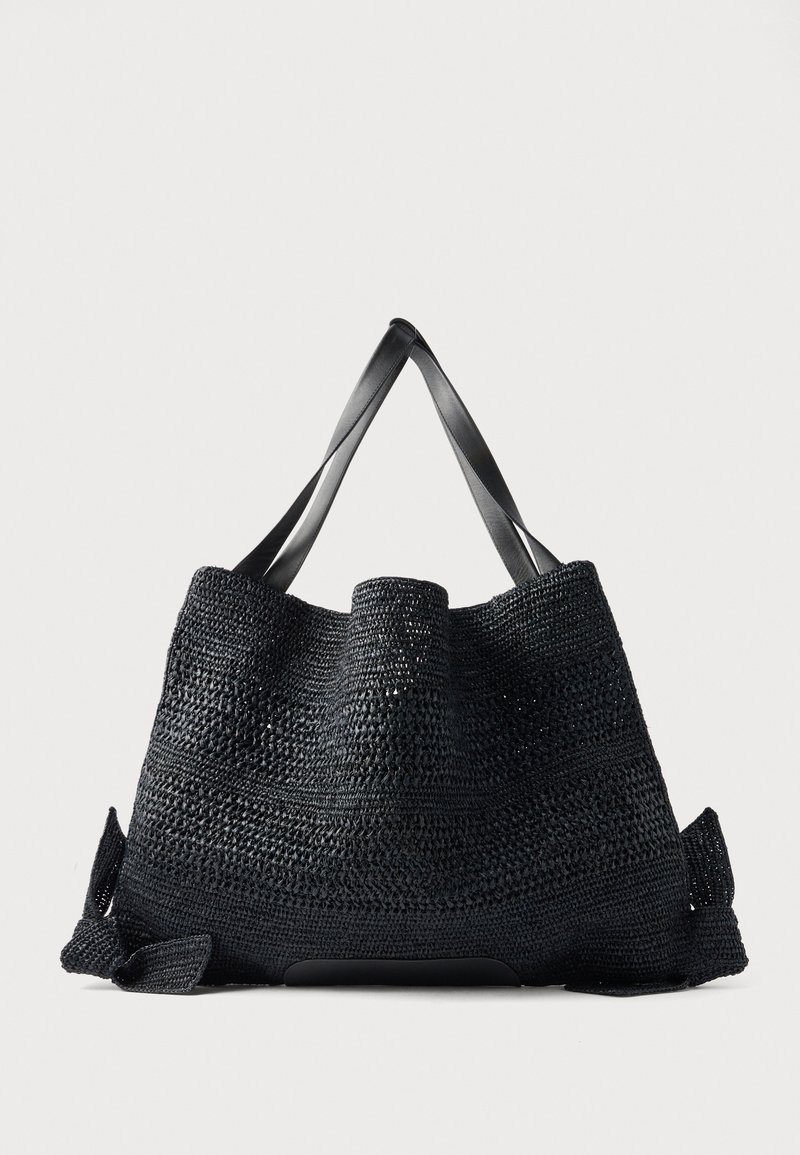 Μεγάλη μαύρη υφαντή τσάντα ώμου με φαρδιές επίπεδες λαβές και ανοιχτό πάνω μέρος, τοποθετημένη σε απλό φωτεινό φόντο.