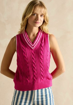 Fuchsia knit sleeveless vest with cable patterns and a shawl collar featuring white stripes. Paired with blue and white striped pants.
