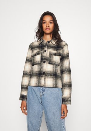 Plaid jacket made of soft fabric in cream, black, and gray tones. Features chest pockets, button closure, and a classic collar design.