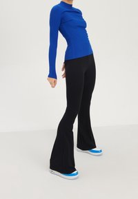 Haut bleu côtelé à manches longues avec un col montant et une silhouette ajustée, assorti à un pantalon noir évasé. Des baskets bleu et blanc complètent le look.