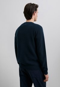 Navy blue knitted sweater with ribbed cuffs and hem, featuring a crew neck and a textured fabric. Back view shows seamless design.