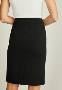 Černá tužková sukně z hladkého materiálu; má rovný střih, zadní rozparek a nenápadné zapínání na zip se smyčkovým akcentem.