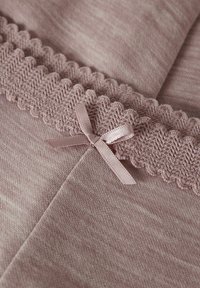Blødt pink stof med en tekstureret, scallop trim og en lille satinbue, der fremhæver kanten. Glat overflade, letvægtsmateriale.