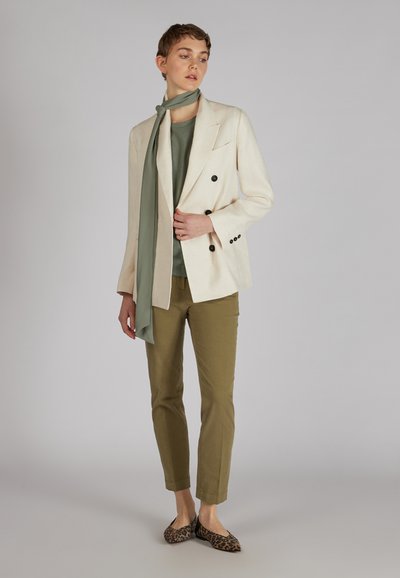 Dopasowana kremowa marynarka z czarnymi guzikami, zielony szalik, oliwkowe spodnie i baleriny w panterkę, prezentujące miks faktur i kolorów.