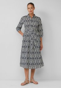 Marineblaue und cremefarbene Kleid mit Blattmuster, Kragen, Dreiviertelärmeln und gebundenem Taillenband. Kombiniert mit metallischen flachen Sandalen.