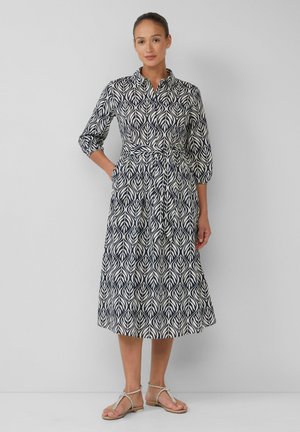 Marineblaue und cremefarbene Kleid mit Blattmuster, Kragen, Dreiviertelärmeln und gebundenem Taillenband. Kombiniert mit metallischen flachen Sandalen.