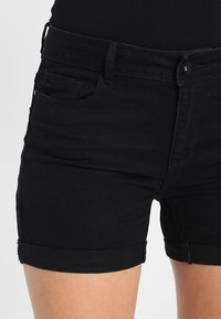 Černé džíny kraťasy s přiléhavým střihem, ohrnutými manžetami a klasickým pětipocket stylem. Materiál má mírnou texturu a pevné švy.