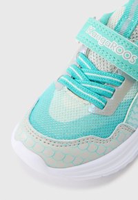 Αθλητικό παπούτσι με υδάτινο θέμα, με επάνω μέρος από τυρκουάζ δίχτυ, ασημένιες λεπτομέρειες και μοτίβο που μοιάζει με λέπια. Διαθέτει ελαστικά κορδόνια και ιμάντα με βέλκρο.