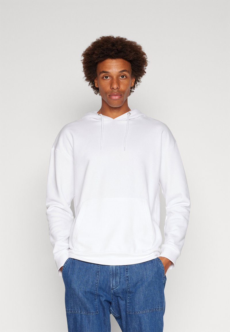 Felpa bianca con cappuccio, tasca a marsupio, cordini e polsini a coste, abbinata a jeans blu. Tessuto morbido e liscio.