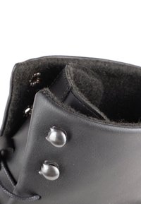 Stivale in pelle nera con colletto arrotondato, dotato di hardware in argento e una morbida fodera interna scura. Esterno testurizzato con lacci.