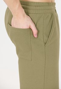 Olivgrön, bomullsbyxor för avkoppling har en elastisk midja, sidficka och en mjuk textur. Designen betonar komfort och funktion.