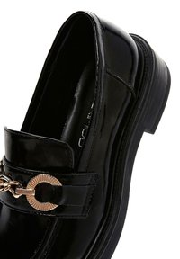 Schwarze Lackleder-Loafers mit einem goldfarbenen Kettenakzent, runder Zehenform und strukturiertem Gummisohle.