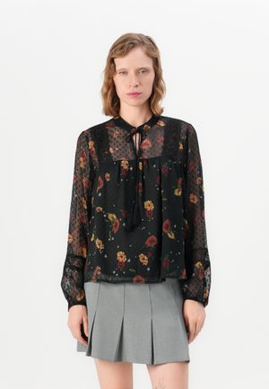 Svart gjennomsiktig bluse med blomstertrykk, prikkete tekstur og rund halslinning. Har lange ermer og en knyttedetalj ved halsen.