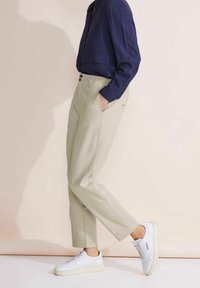 Beiga skräddarsydda byxor med rak passform, sidofickor och subtila sömmar. Kombinerat med en marinblå långärmad skjorta och vita sneakers.