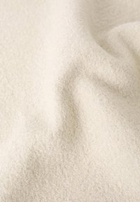 Tissu beige clair avec une finition douce et texturée, affichant une surface subtile et duveteuse, doucement drapé pour révéler sa qualité lisse et souple.