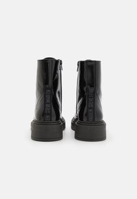 Black patent leather ankle boots with a chunky black sole, side zippers, and embossed branding on the back pull tabs.