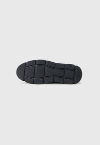 Semelle de chaussure en caoutchouc noir avec un motif en grille et une texture variable. Présente un logo au centre et une pointe arrondie pour une meilleure adhérence.