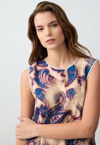 Ärmelloses Top aus leichtem Material mit beiger Basis, das ein wirbelndes blaues und burgunderfarbenes Blumenmuster aufweist. Runder Ausschnitt und schlanker Schnitt.