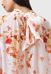 Bloemenblouse in lichtgewicht, doorschijnende stof met een witte basis. Heeft meerkleurige bloemen, een gerimpelde halslijn en een strik aan de achterkant.
