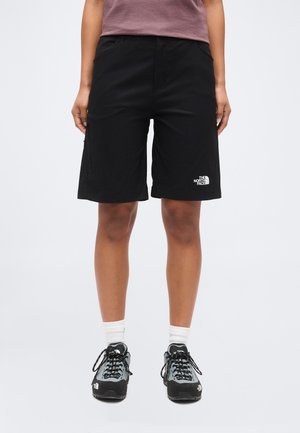 Person iført sorte The North Face knælange shorts, hvide sokker og sorte og grå vandresko, stående mod en hvid baggrund.