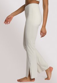 Witte uitlopende leggings van rekbaar materiaal met zijsplitten aan de onderkant, voorzien van een hoge tailleband en een gladde textuur.