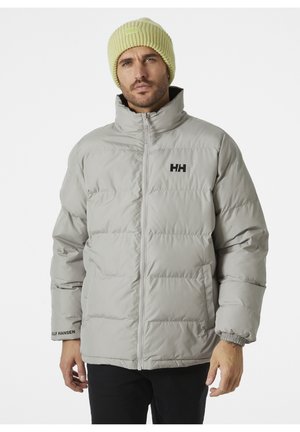 Lichtgrijze pufferjack met hoge kraag, zichtbare stiksels en het "HH"-logo op de borst. Draagt een getextureerde lichtgele beanie.