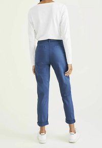 Pantalons en coton bleu avec des ourlets retroussés, deux poches arrière, associés à un haut à manches longues blanc et des baskets blanches. Texture lisse.