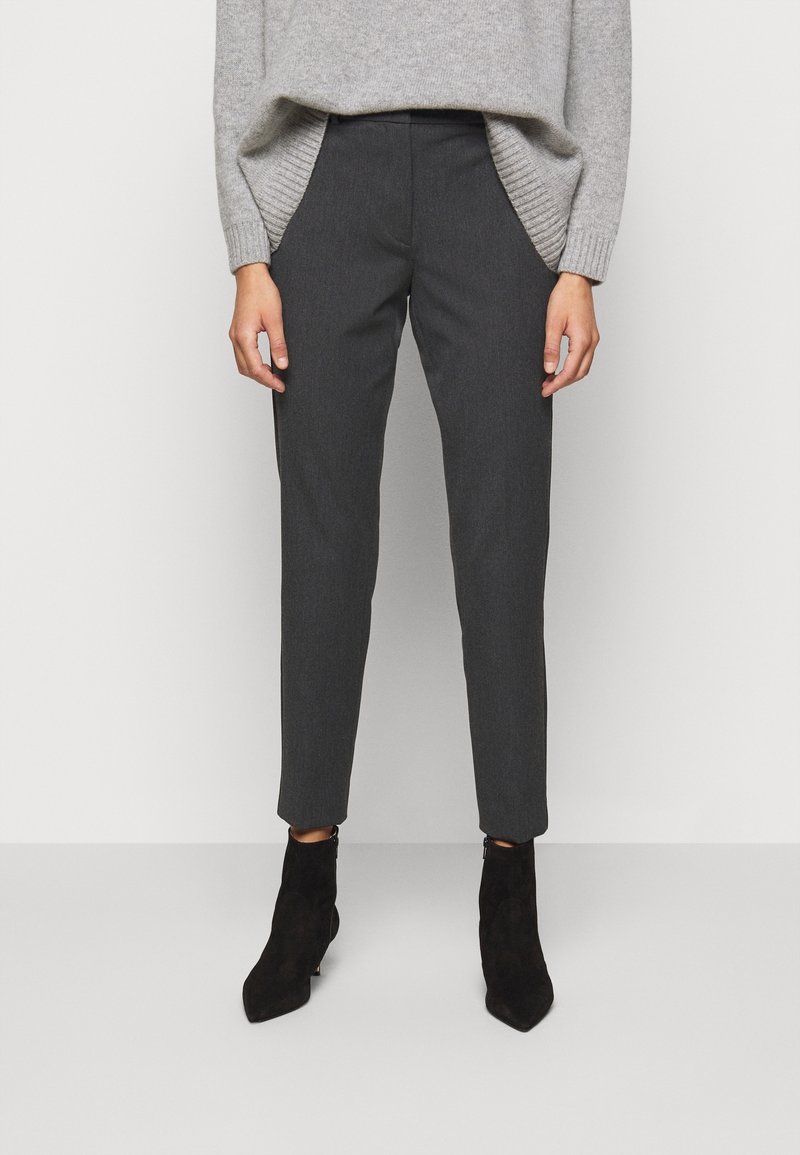 Pull en maille grise superposé sur un pantalon tailleur gris foncé. Le pantalon présente une coupe slim et des poches. Des bottines noires à bouts pointus complètent le look.