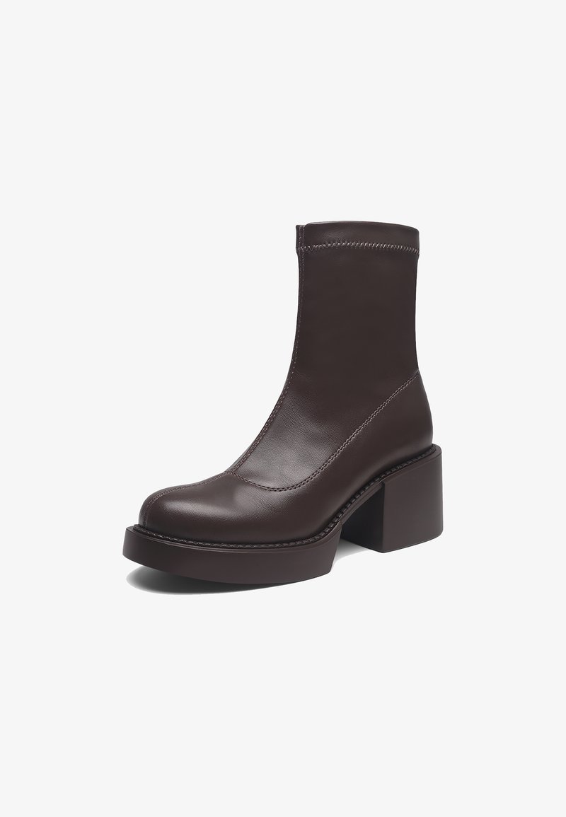 Bota de tobillo de cuero marrón con un tacón bloque, que presenta una textura suave y detalles de costuras a lo largo de las costuras. Diseño elegante y minimalista.