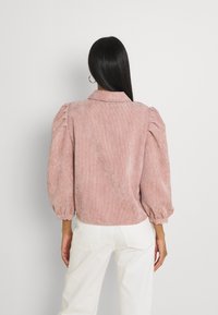 Rosa kordflorsblus med puffärmar och krage. Har ribbad yta och elastiska muddars. Matchas med vita byxor.