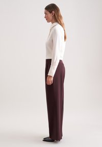 Crème blouse met lange mouwen en geknopen manchetten, gecombineerd met hoog-gewelfde, wijde bordeauxrode broek en zwarte platte schoenen; gladde stoftextuur.