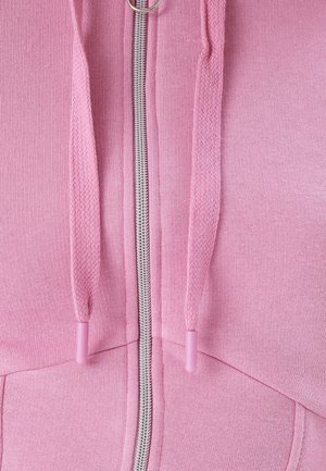 Vaaleanpunainen vetoketjullinen huppari, jossa on hopeanvärinen vetoketju, teksturoitu nyöri vastaavilla päillä ja pehmeä kangaspinta.